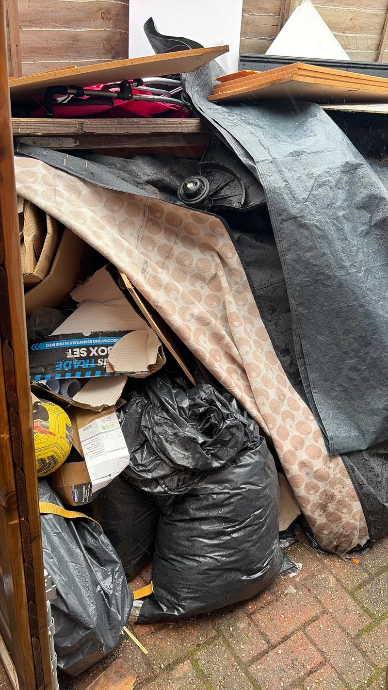 Mixed waste including bags and household items in an outbuilding